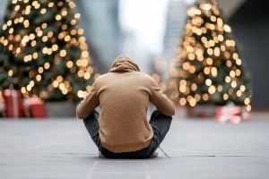 A man sits on the ground in front of a Christmas tree